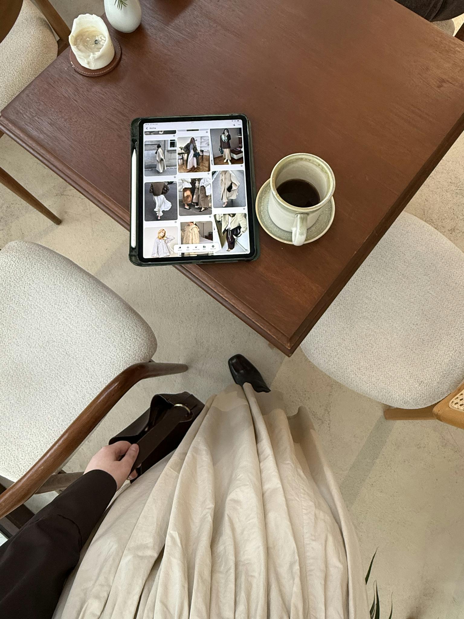 Top-down view of person browsing fashion on tablet with coffee at a cozy cafe table.